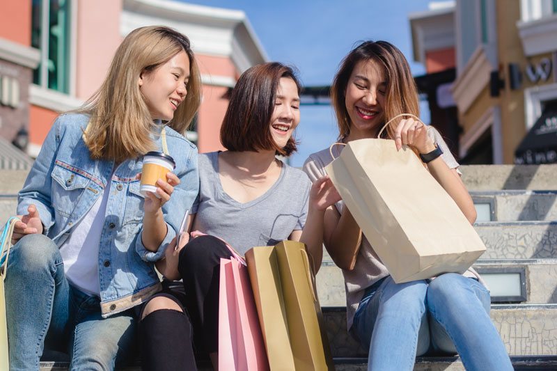 Three friends sitting on steps with shopping bags
